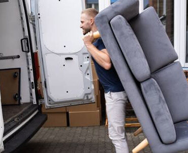 Möbellift Kaiserslautern: Helfer tragen ein graues Sofa aus einem Transporter